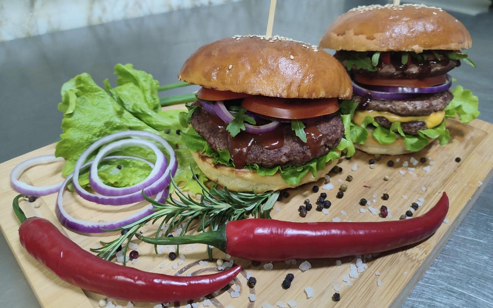 Dwa kraftowe burgery wołowe na desce z warzywami i papryczkami chili